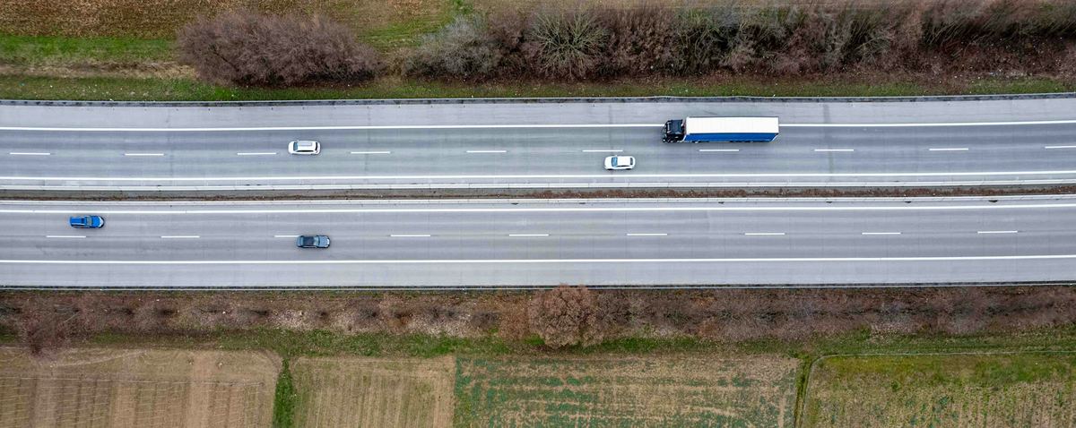 Luchtfoto van een snelweg met twee rijbanen, een vrachtwagen met oplegger en enkele wagens, tussen akkers